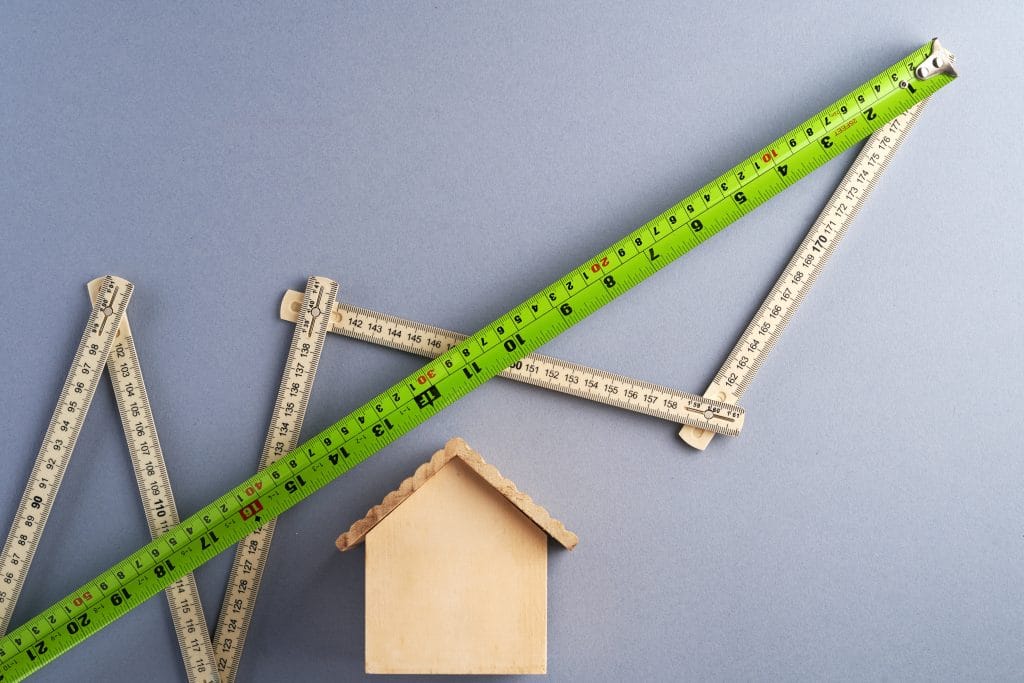 image with two measuring tapes around a small wooden house.