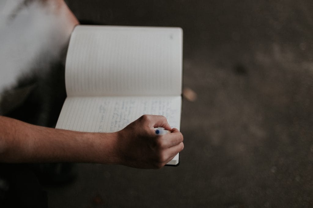 A person takes notes in a lined notebook with a blue ink pen.