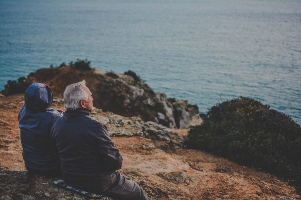 Visto D7 em Portugal - Everything you need to know. The picture shows an elderly couple sitting on one of the cliffs on the coast of Lagos, Algarve.