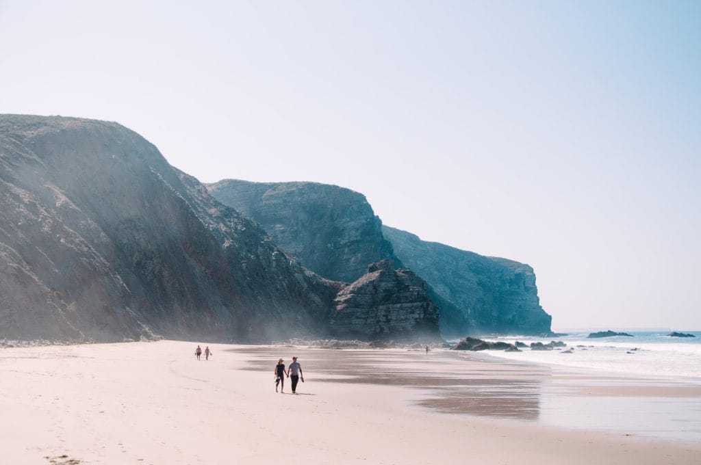 image from the article “D8 Visa for Digital Nomads 2026”. The image shows a couple walking along the sandy shore of Arrifana Beach in the Algarve.