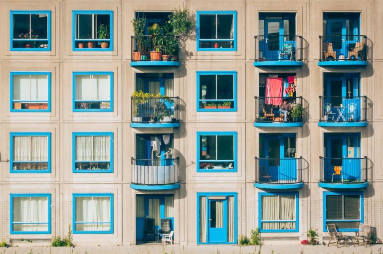 article cover image: Everything about Condominiums. In the picture, several windows and balconies are painted blue, with plants, chairs, and clothes.